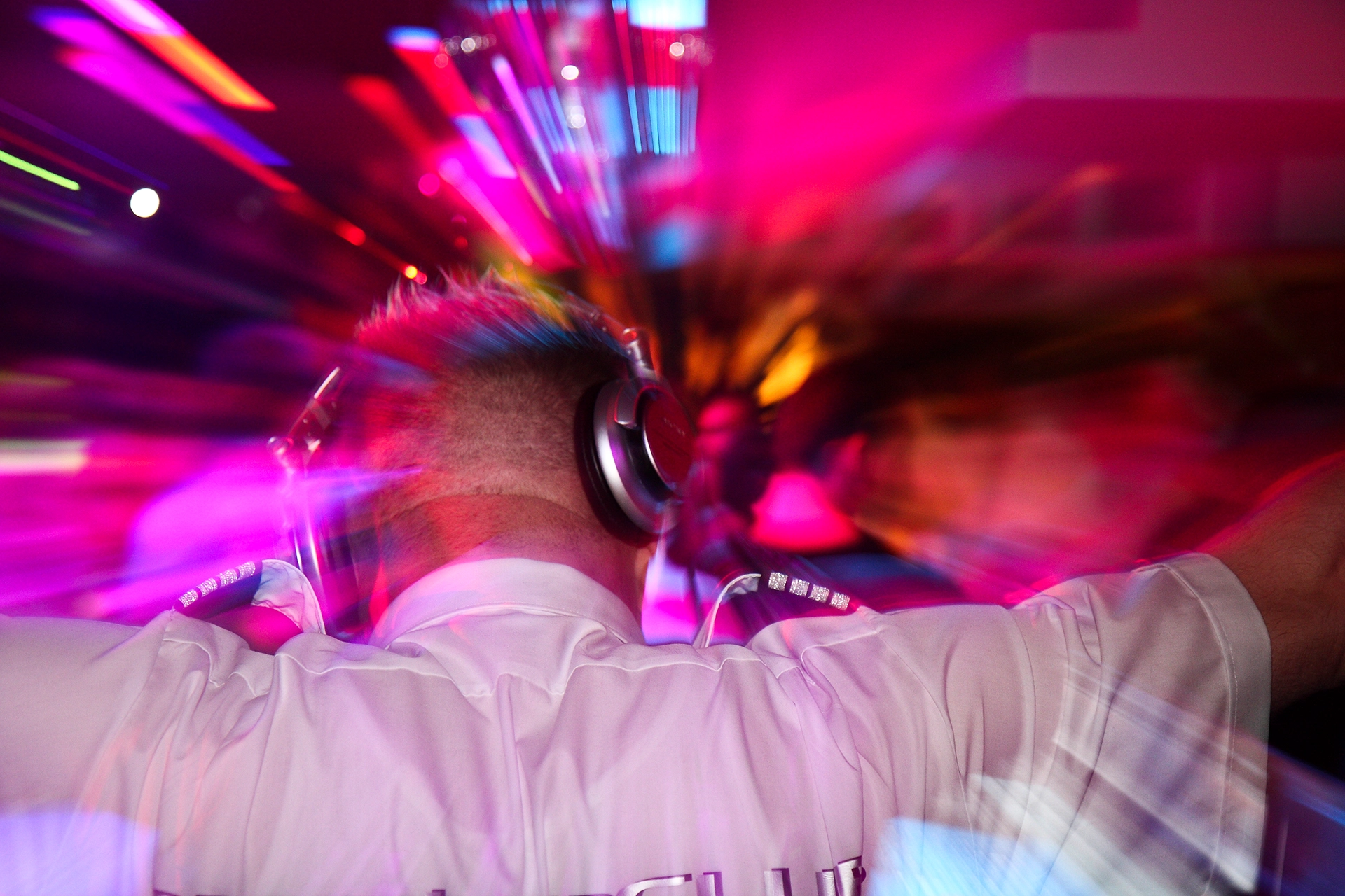 DJ Frank Woiton Hyping the crowd with raised arms while colorful enlightend.